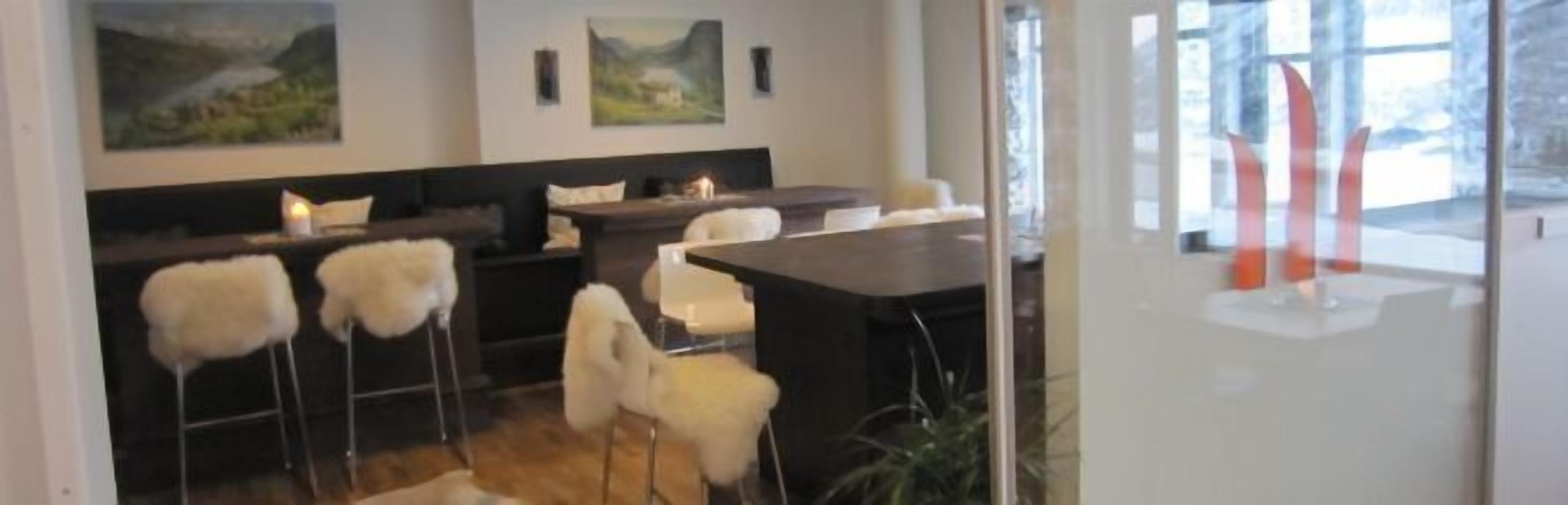 A modern interior with a bar area, white fluffy chairs, and artwork on the walls.