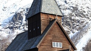 A wooden church with a steeply pitched roof and a bell tower, set against a snowy mountain backdrop. - Hordatun Hotel (Ullensvang)