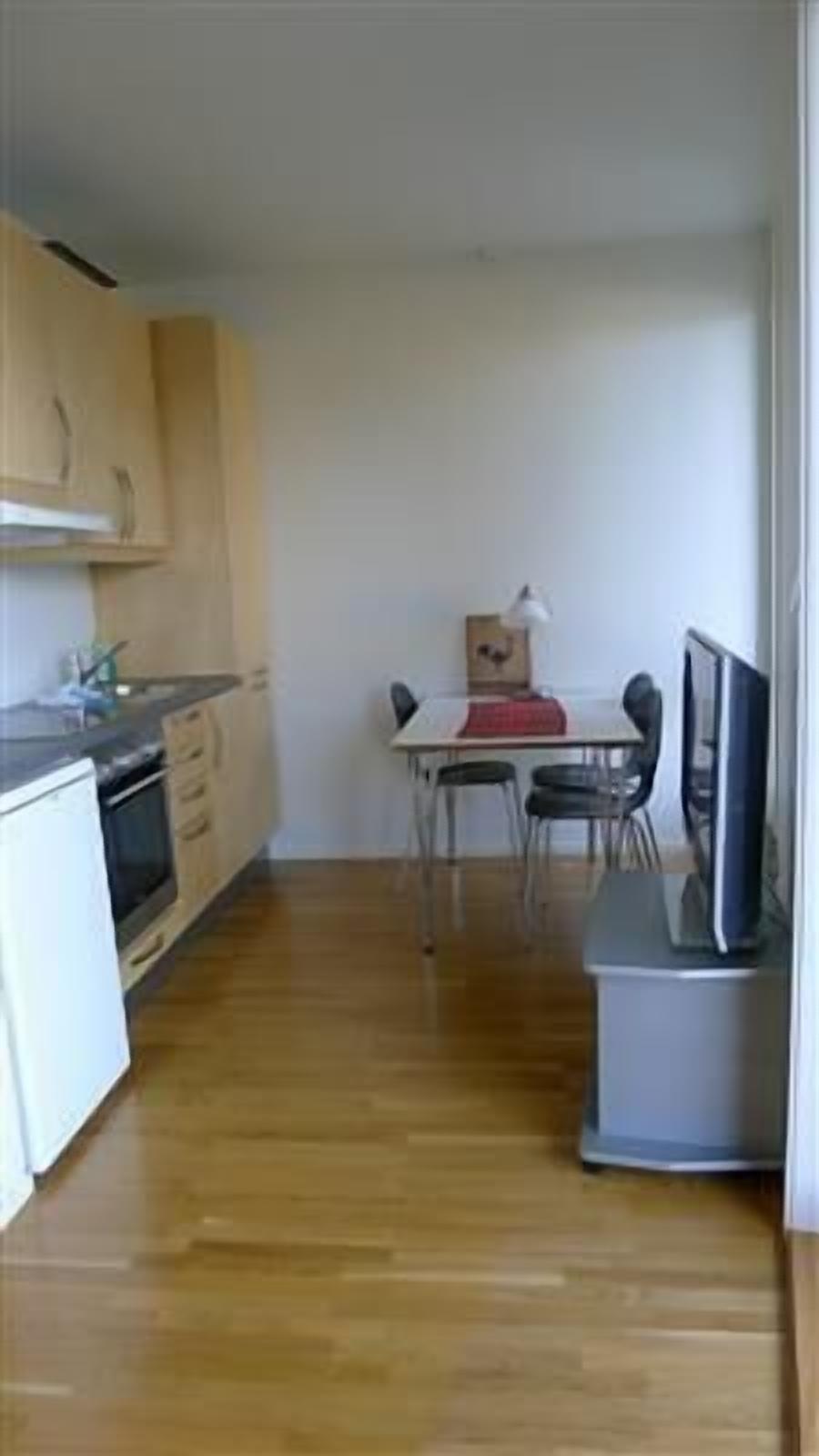 A compact kitchen with wooden cabinets, a dining table with chairs, and a small TV.