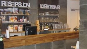A reception area with a counter, shelves with magazines and snacks, and a bar area with glasses and bottles. - Hordatun Hotel (Ullensvang)