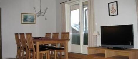 A dining area with a wooden table and chairs, a television on a wooden stand, and a painting on the wall.