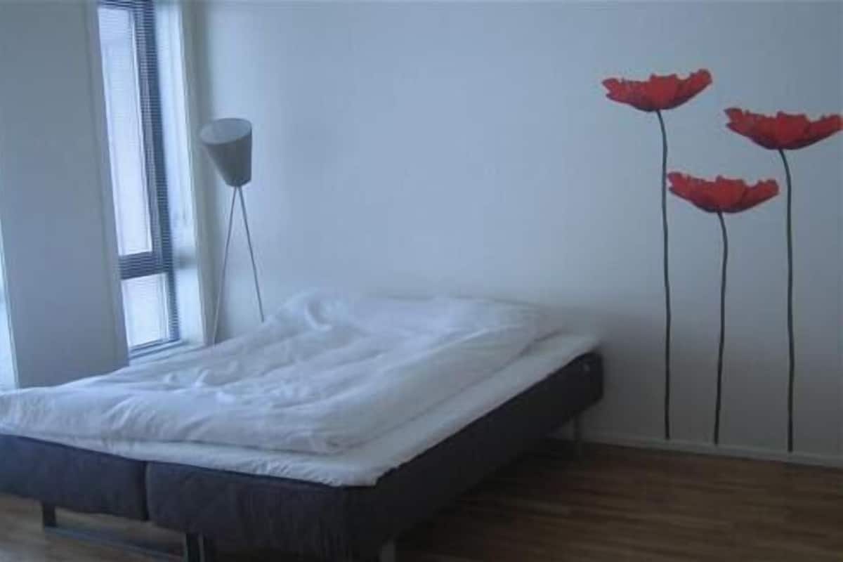 Quarto com cama, janela e parede decorada com flores vermelhas.