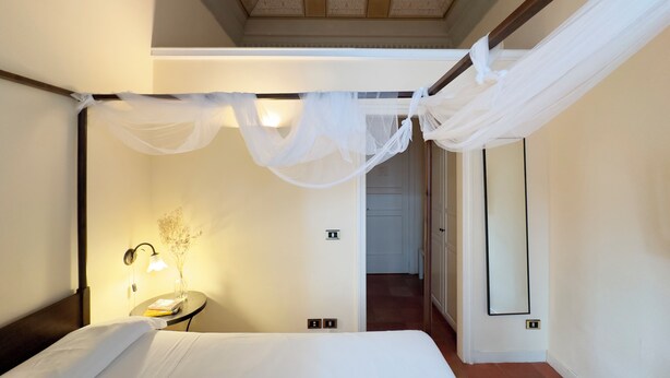 Un dormitorio con cama con dosel, una mesita de noche con lámpara y un espejo en la pared.
