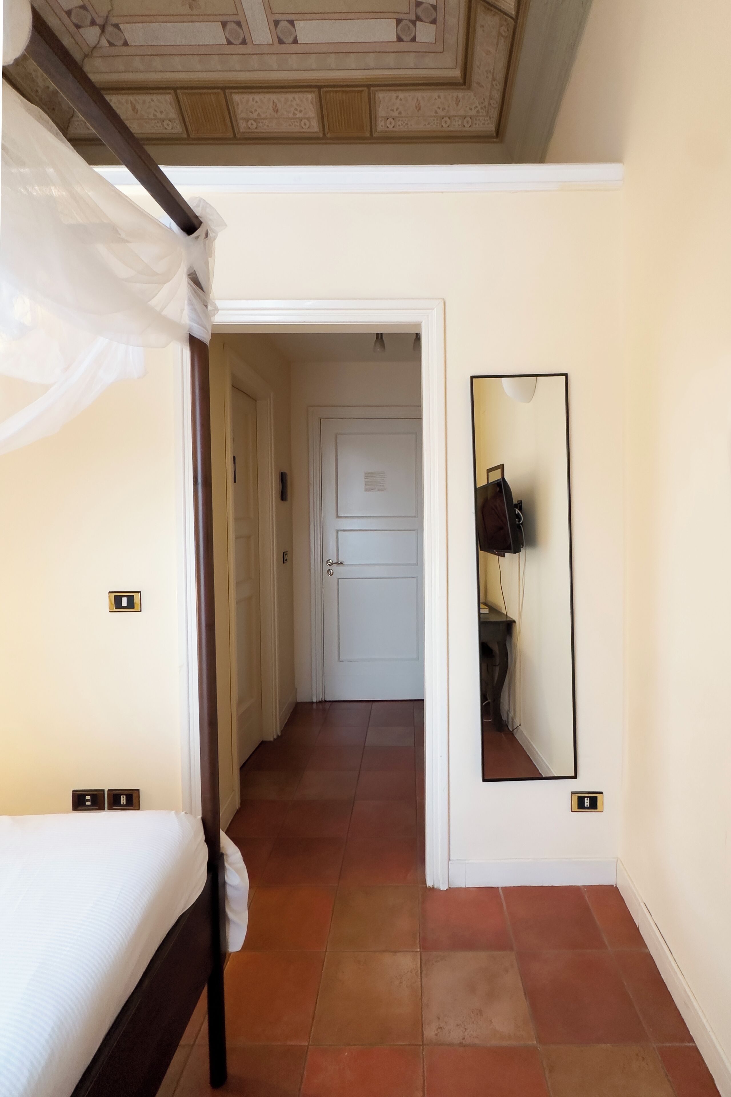 Un dormitorio con cama con dosel, un pasillo que conduce a una puerta y un espejo en la pared.