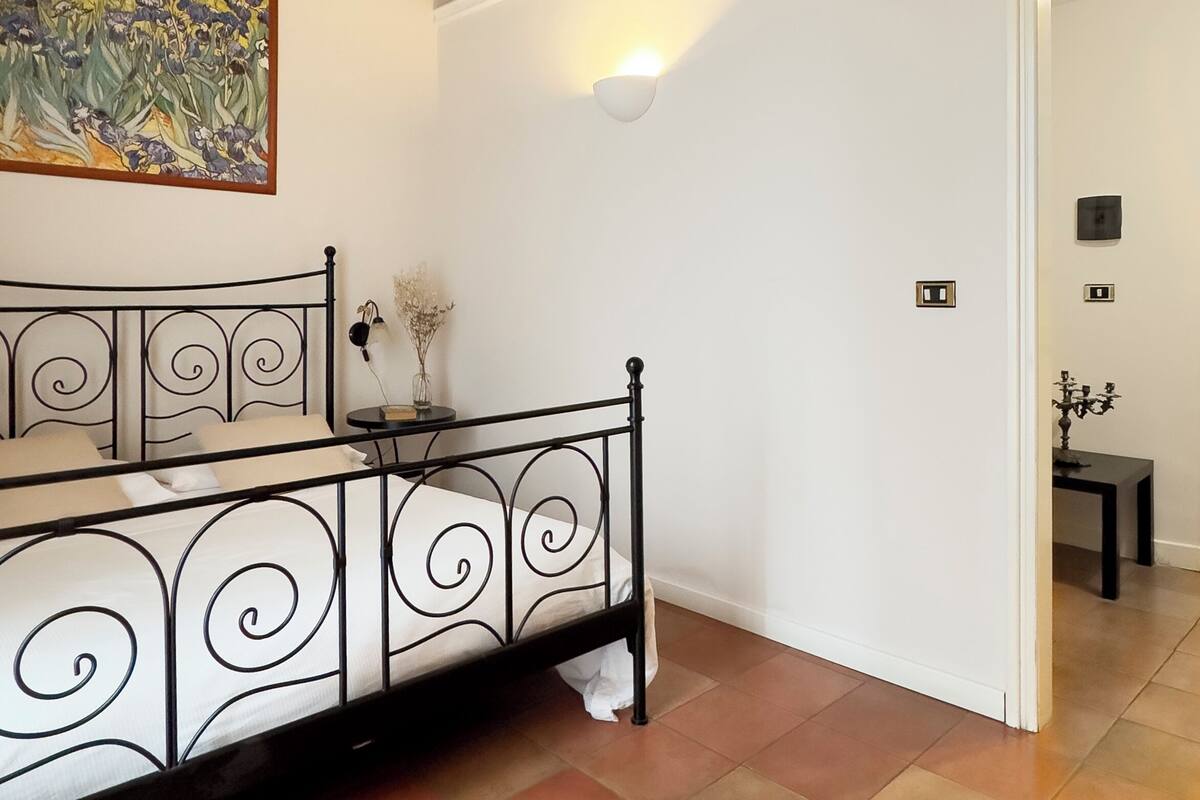 A bedroom with a bed, a painting, and a wall-mounted light fixture.