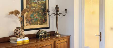 Un gabinete de madera con un cuadro enmarco, un jarrón con flores secas y un candelabro.