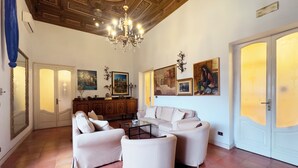 Amplia sala de estar con candelabro, sofás blancos, una mesa de centro y obras de arte en las paredes.