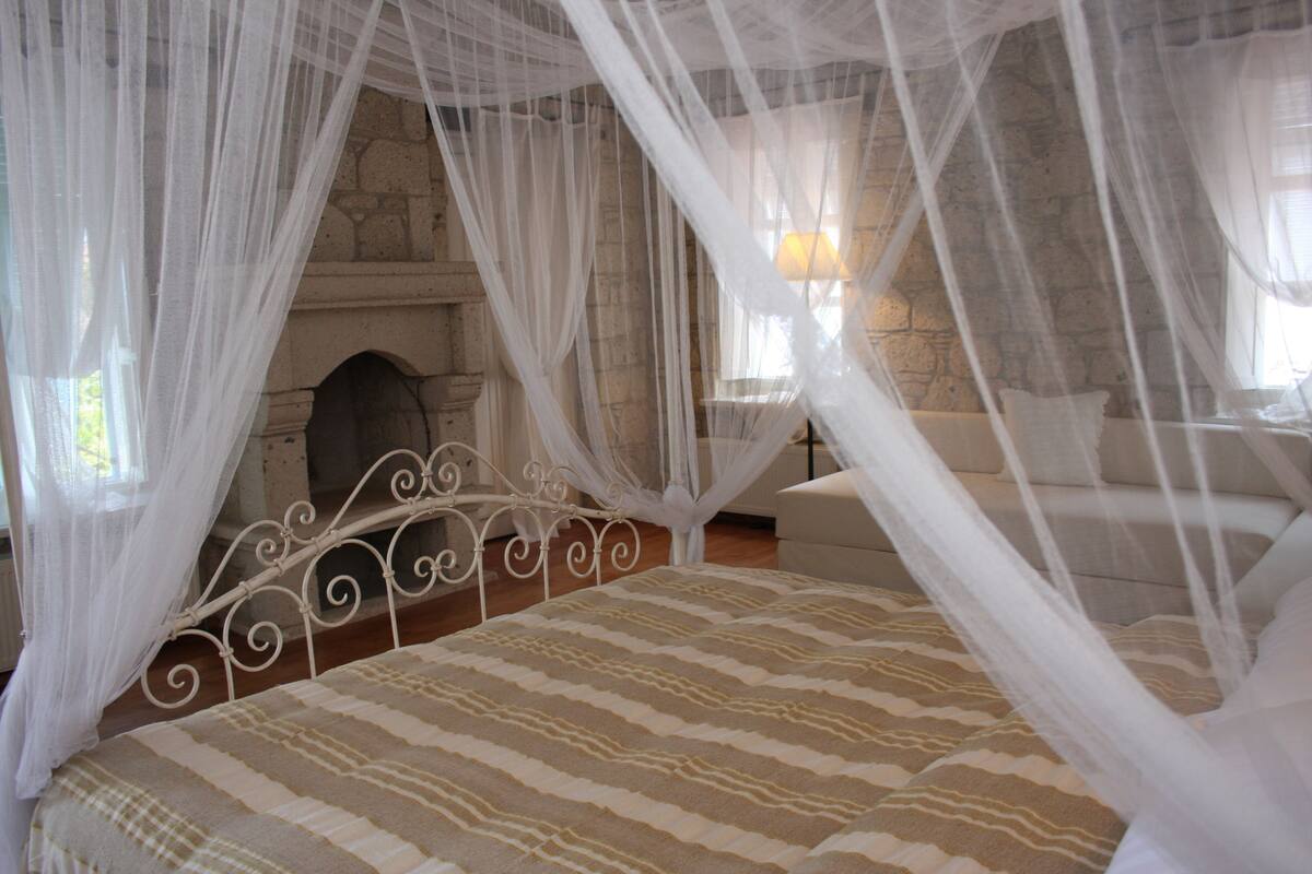 A bedroom with a bed under a canopy, a stone fireplace, and a sofa.