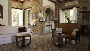 A living room with a stone wall, a white sofa, a brown armchair, and a patterned floor. - Incirliev - Special Class (Cesme)