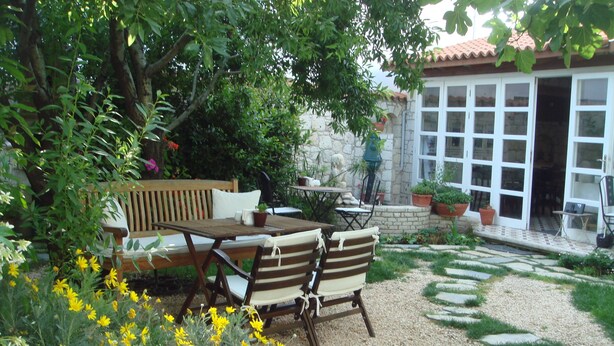 A patio with a wooden table and chairs, surrounded by potted plants and yellow flowers. - Incirliev - Special Class (Cesme)