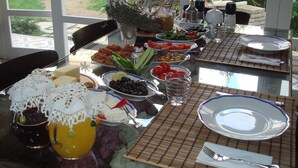 A dining table set with various dishes, glasses, and utensils, with a view of a garden through large windows. - Incirliev - Special Class (Cesme)