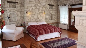A bedroom with stone walls, a bed with a red and white striped blanket, a white armchair, and a wooden floor. - Incirliev - Special Class (Cesme)