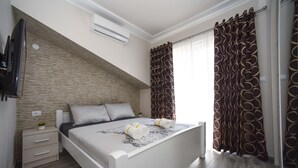 Ein Schlafzimmer mit Bett, Nachttisch, Fernseher und einem Fenster mit Vorhängen.
