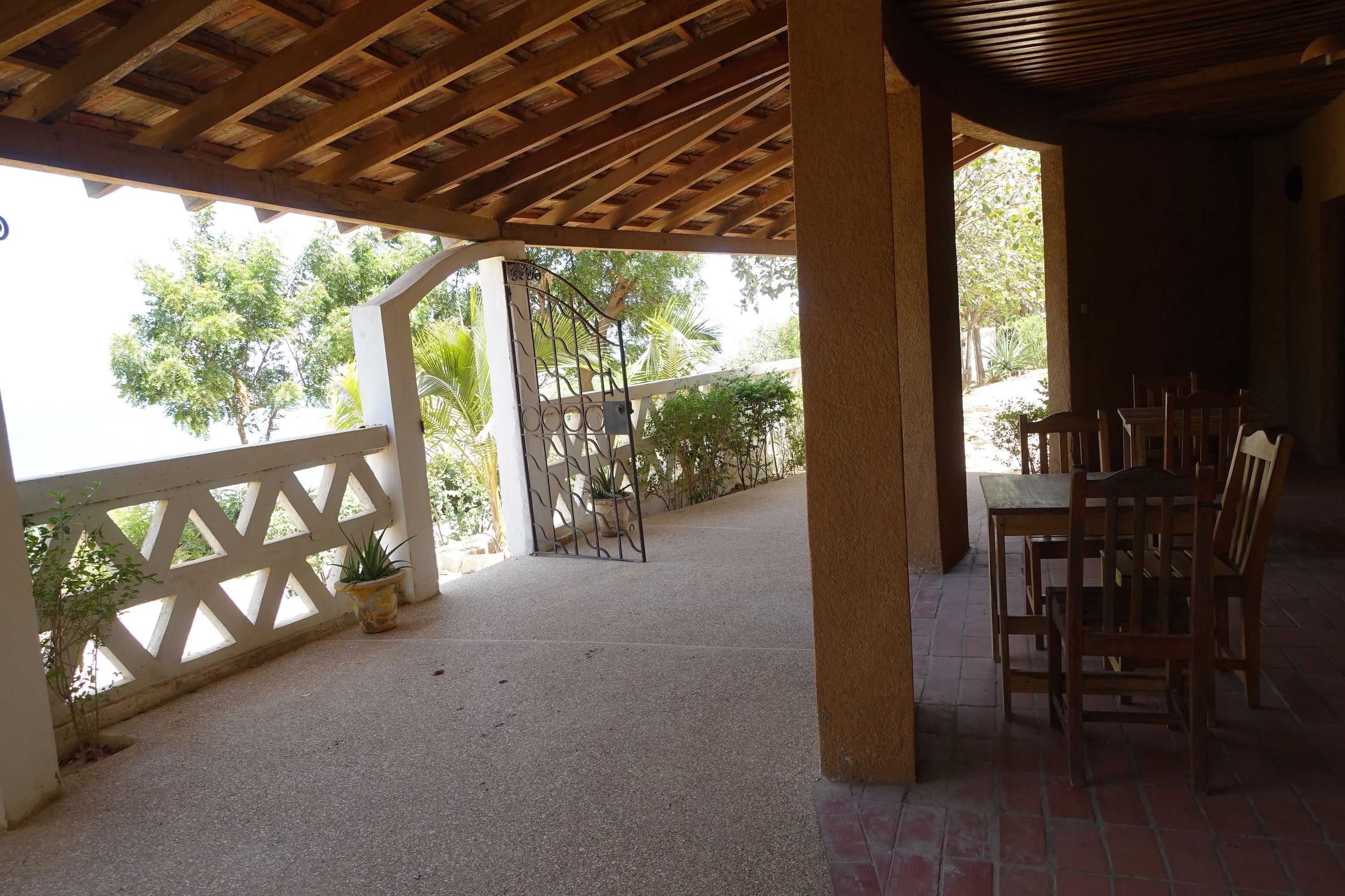 Eine überdachte Terrasse im Freien mit Holzboden, einem weißen Gitterzaun und einem Esstisch mit Stühlen.