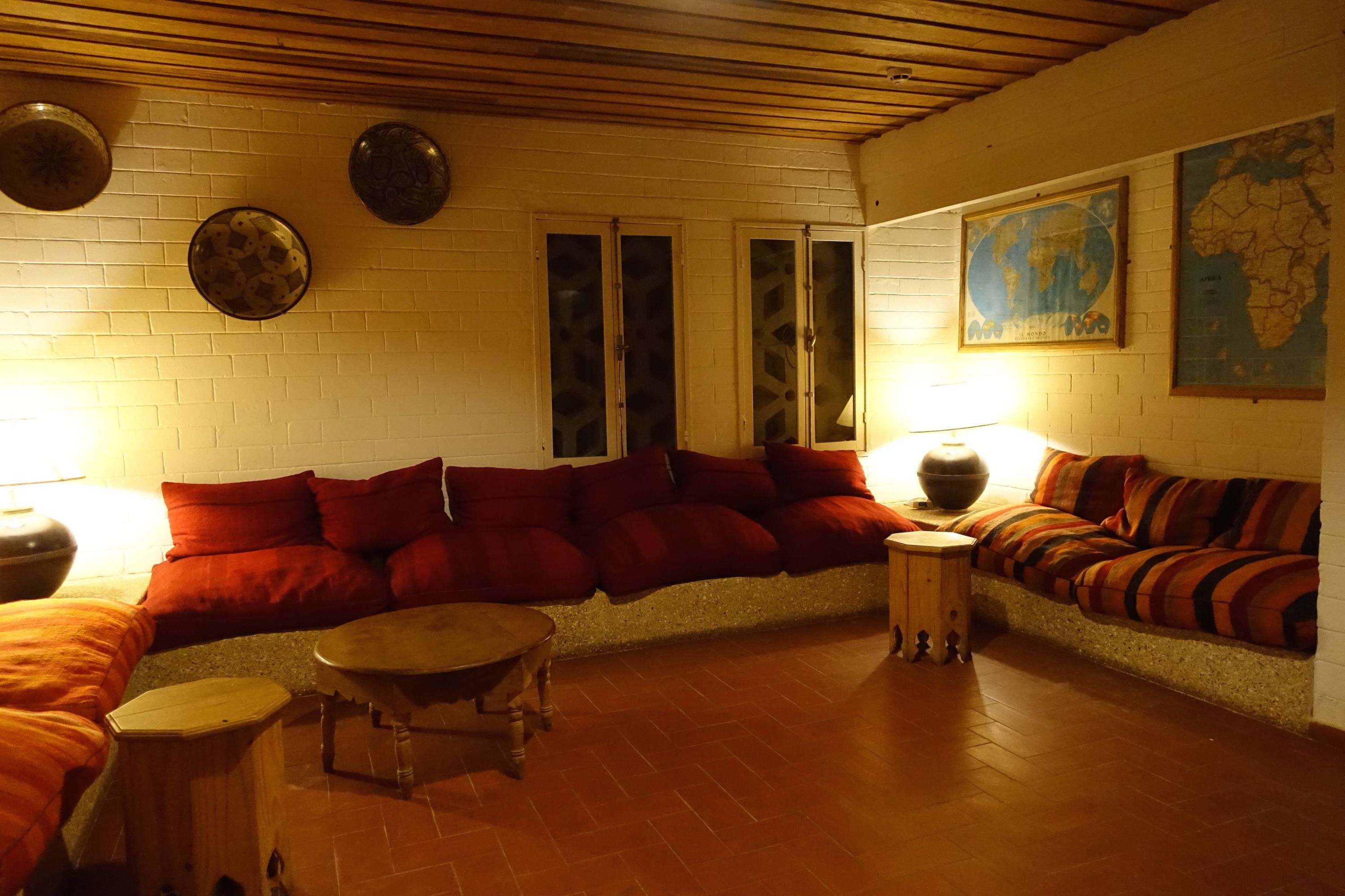 A cozy living room with a curved sofa, a round coffee table, and a small wooden stool. There are two doors with glass panels and a map on the wall.