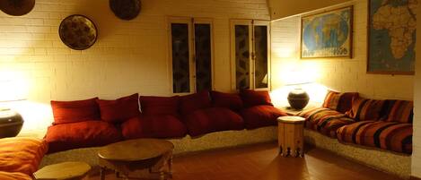 A cozy living room with a curved sofa, a round coffee table, and a small wooden stool. There are two doors with glass panels and a map on the wall.
