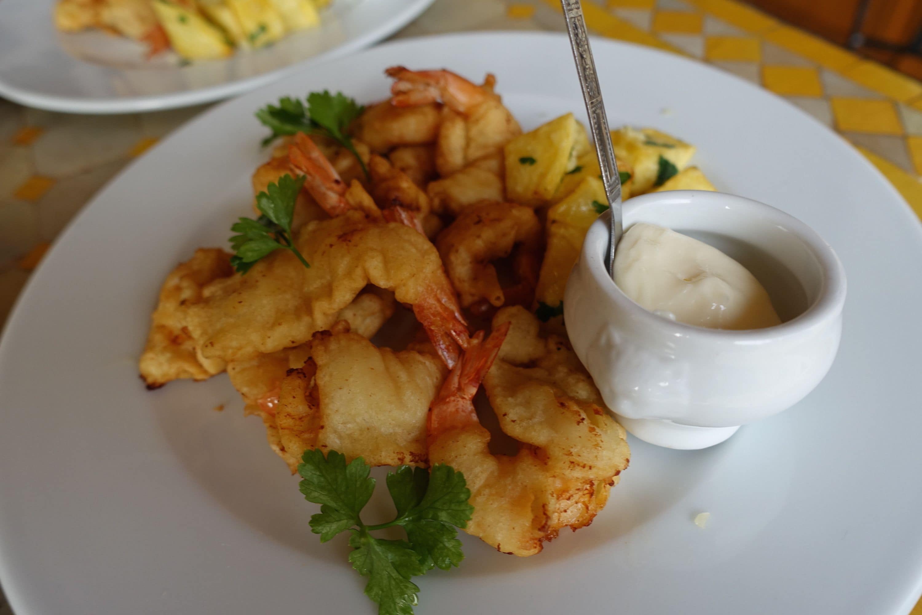 A plate of fried shrimp and potatoes with a small bowl of sauce.