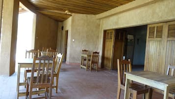 Un patio amplio con mesas y sillas de madera, piso de baldosas y techo de madera.