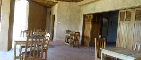 A spacious patio with wooden tables and chairs, a tiled floor, and a wooden ceiling.