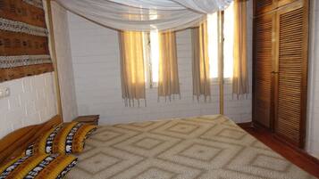A bedroom with a bed, curtains, a window, and a wardrobe.