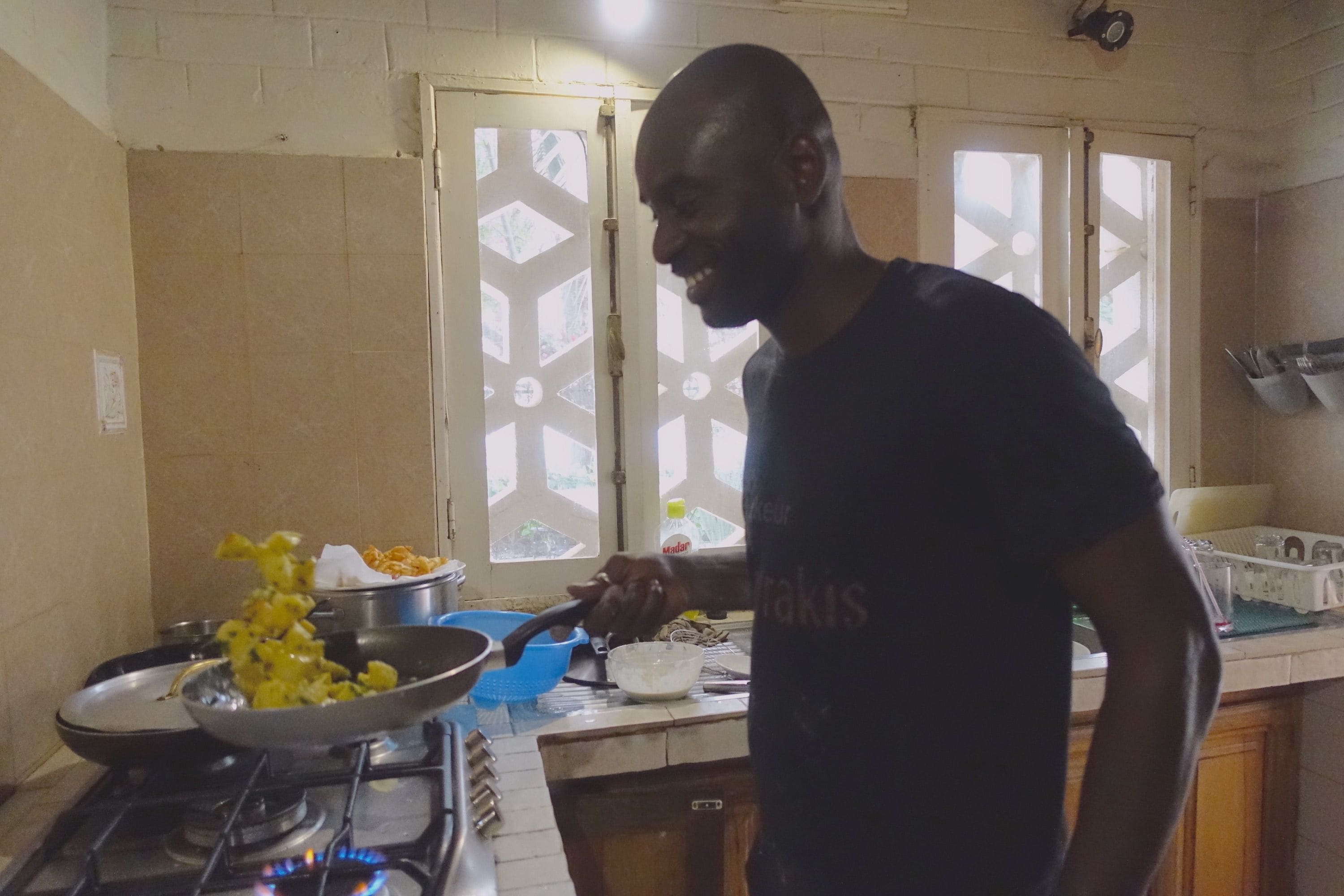 Una cocina con estufa a gas, una sartén, un colador azul y una persona cocinando.