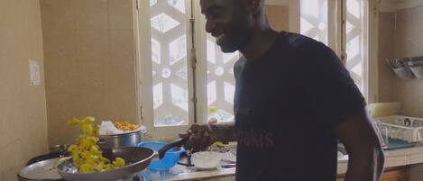 Una cocina con estufa a gas, una sartén, un colador azul y una persona cocinando.