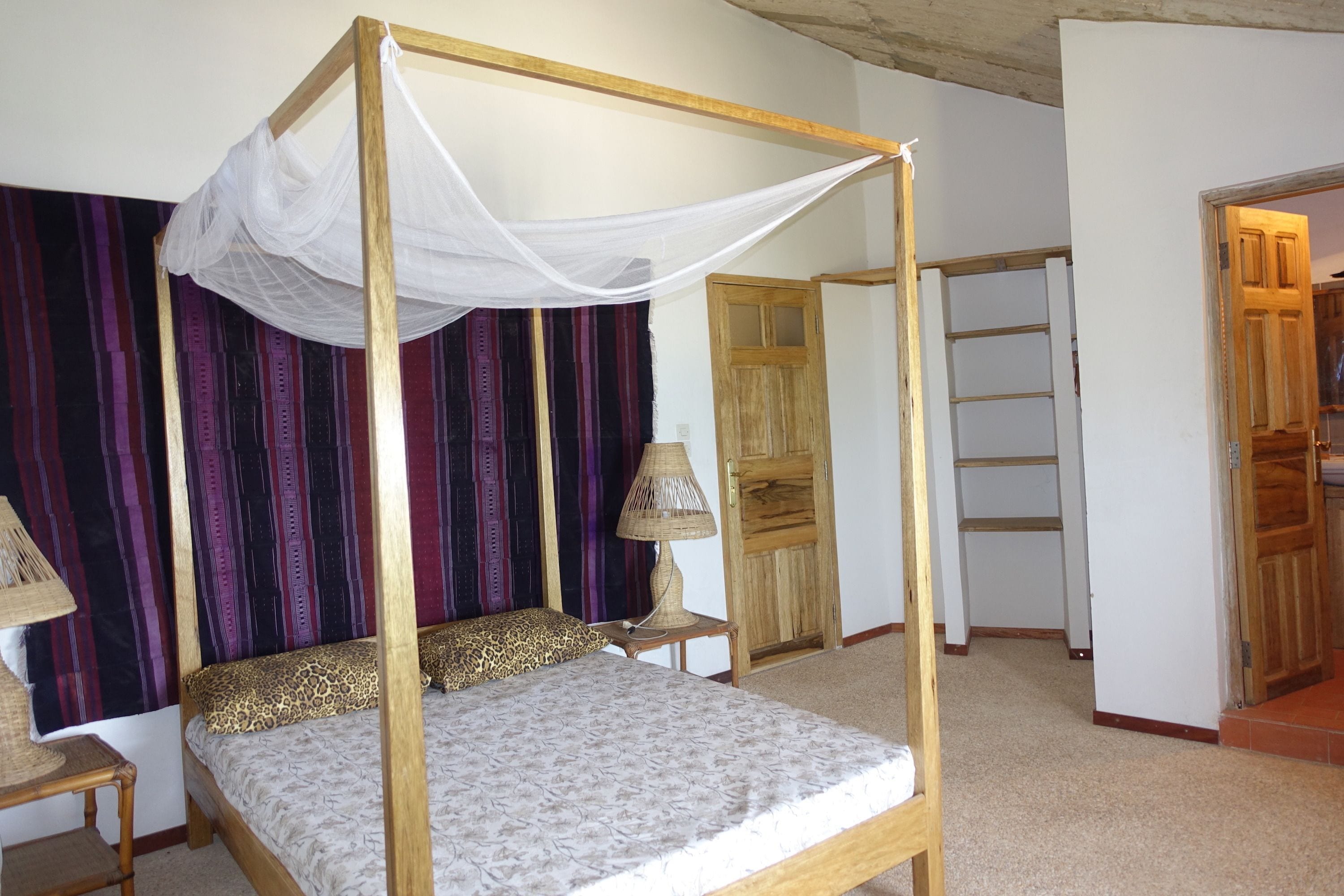 A four-poster bed with a canopy, a wooden wardrobe, and a small bedside table with a lamp.