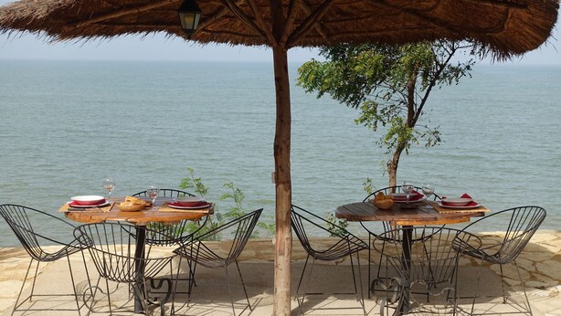 Two tables with chairs and a thatched umbrella, set against a body of water. - Keur Marrakis (Mbour)