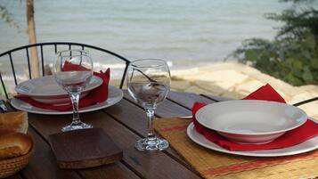 Ein Tisch mit weißen Tellern, roten Servietten und Weingläsern mit Blick auf einen Strand.