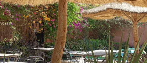 An outdoor patio with thatched umbrellas, metal tables, and chairs.