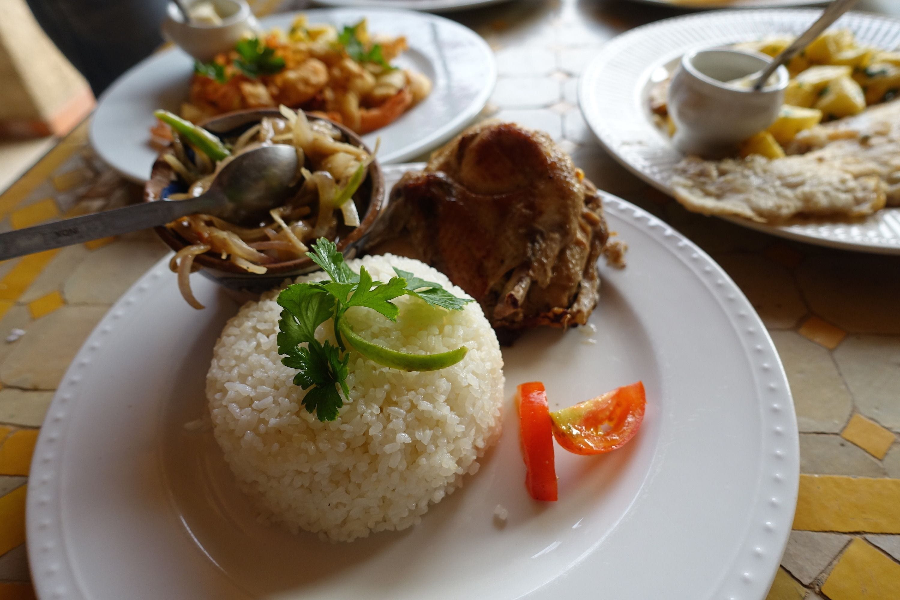 Un plato de comida con arroz, una rodaja de tomate y un trozo de carne, posiblemente pollo, sobre una mesa de baldosas.