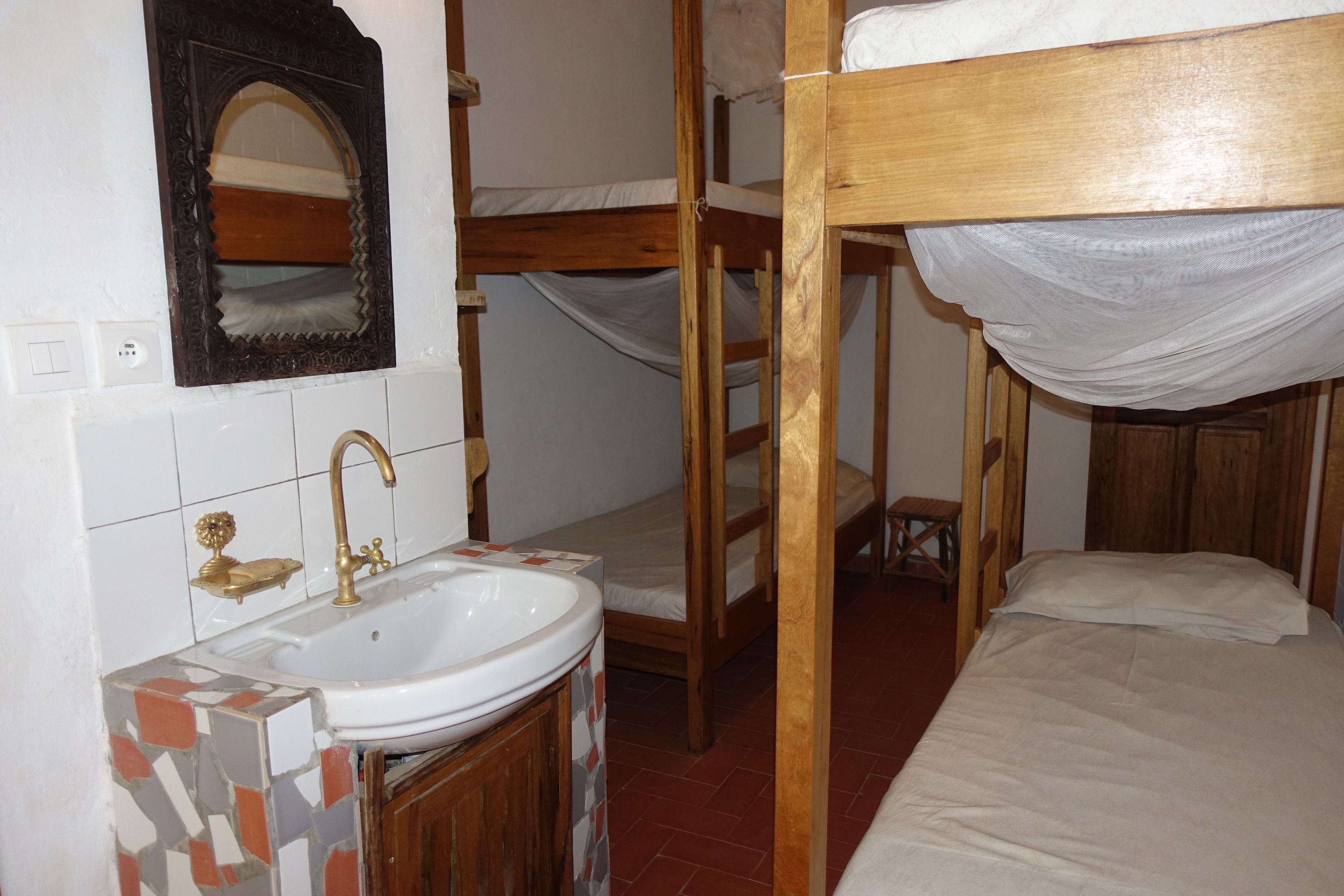 Ein Schlafraum mit Etagenbett aus Holz, einem weißen Waschbecken mit goldfarbenem Wasserhahn und einem Spiegel über dem Waschbecken.