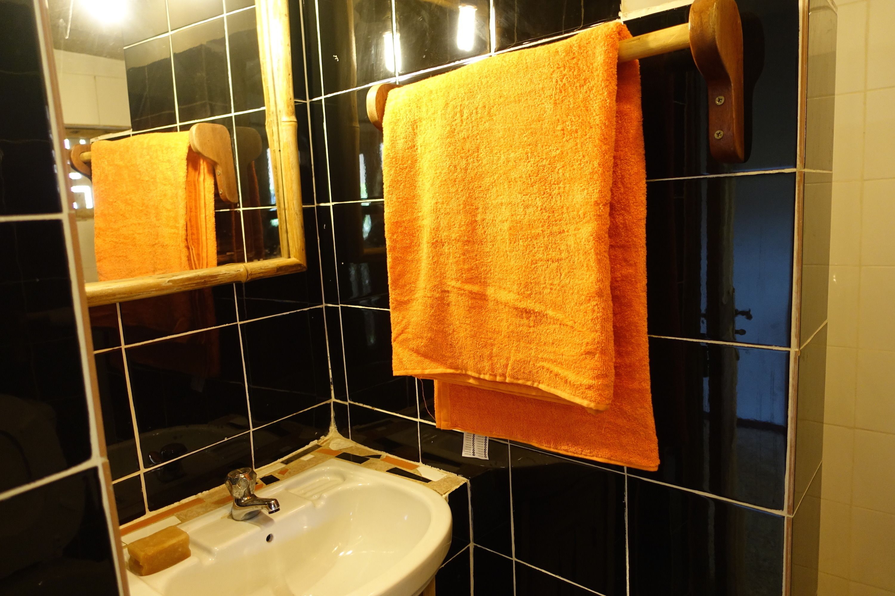 A bathroom with a white sink, black tiled walls, and a wooden towel rack holding an orange towel.