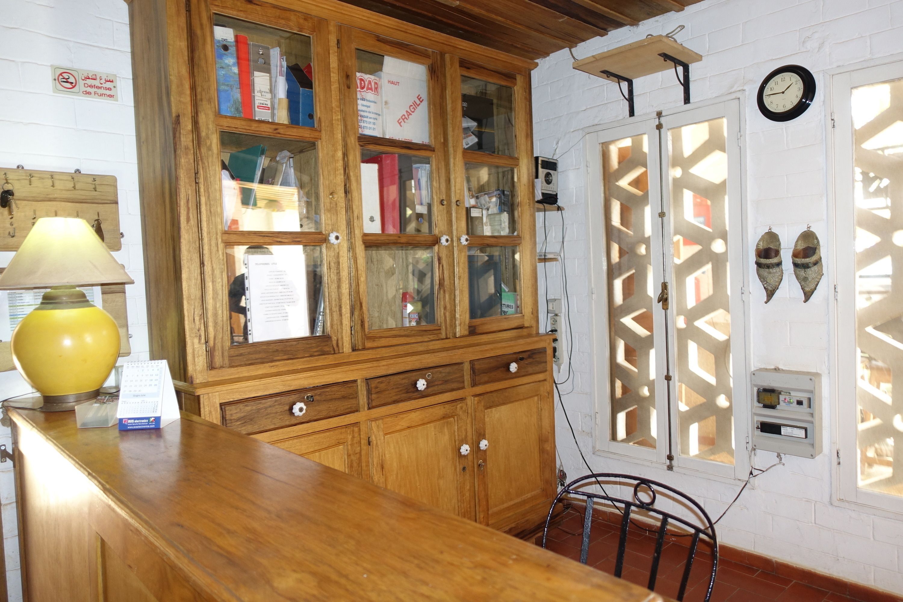 A wooden cabinet with glass doors, a yellow lamp, and a clock on the wall.