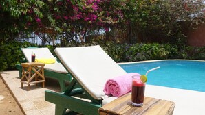 A poolside area with two lounge chairs, one with a pink towel and a drink on a wooden table. - Keur Marrakis (Mbour)