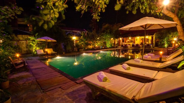 A nighttime pool area with lounge chairs, umbrellas, and a bar area.