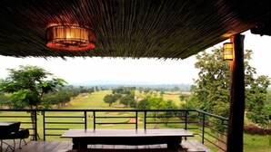 An outdoor patio with a wooden table and chairs, a thatched roof, and a view of a golf course. - Chiangmai Inthanon Golf and Natural Resort (Doi Lo)