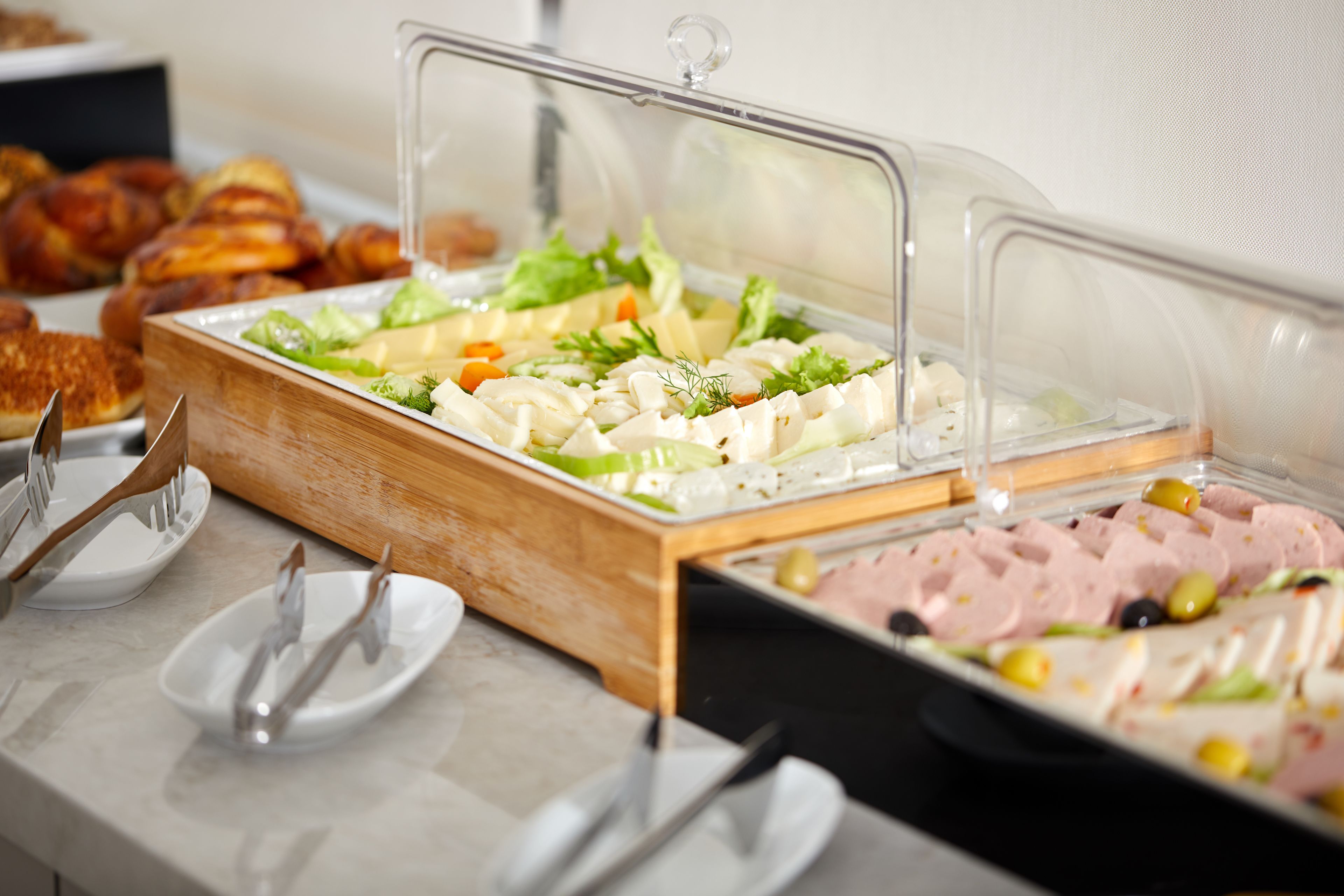 A buffet with various food items, including salads, meats, and cheeses, served on wooden boards with clear plastic covers.