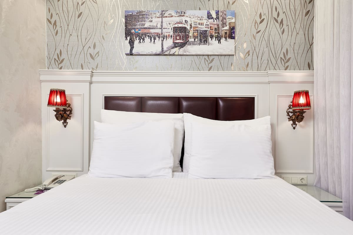 Una habitación de hotel con una cama grande, dos lámparas de noche, un teléfono y un cuadro en la pared.