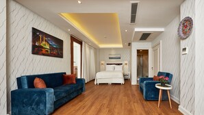 A modern hotel room with a large bed, two blue sofas, a small round table with flowers, and a cityscape painting on the wall. - Albinas Hotel Old City (Istanbul)