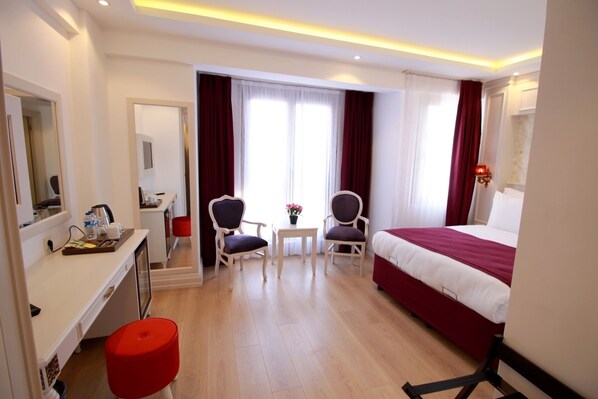 Habitación de hotel con cama, escritorio, sillas y una mesita con un jarrón de flores.