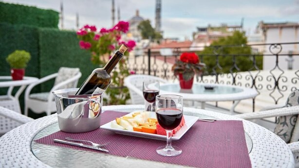 A table with a bottle of wine, glasses, and a plate of food on a balcony. - Albinas Hotel Old City (Istanbul)