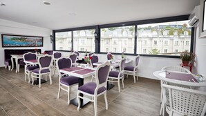 A dining area with white and purple chairs, a large window with a view of buildings, and a painting on the wall. - Albinas Hotel Old City (Istanbul)