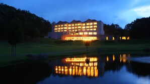 A multi-story hotel with illuminated windows reflecting on a calm body of water. - Nasu Sunlight Hotel (Nasu)