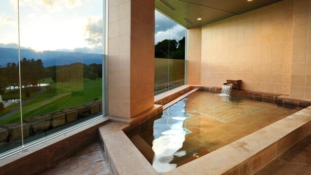 A modern spa with a large glass window, a hot tub, and a view of a golf course. - Nasu Sunlight Hotel (Nasu)