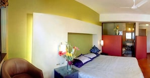 Habitación de hotel con una cama, una silla, una mesita de noche con un jarrón de flores y un baño visible a través de una puerta abierta.