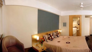 Habitació d'hotel amb sostre corbat, un llit amb edredó beix, una tauleta de nit amb un vas de flors i una cadira.