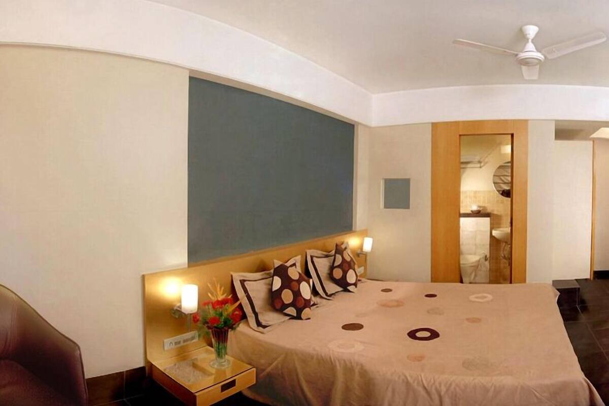 A hotel room with a curved ceiling, a bed with a beige bedspread, a nightstand with a vase of flowers, and a chair.