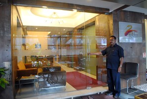 A man standing in a modern hotel lobby with a glass partition, a sofa, and a chair. - Golden Swan (Mumbai)