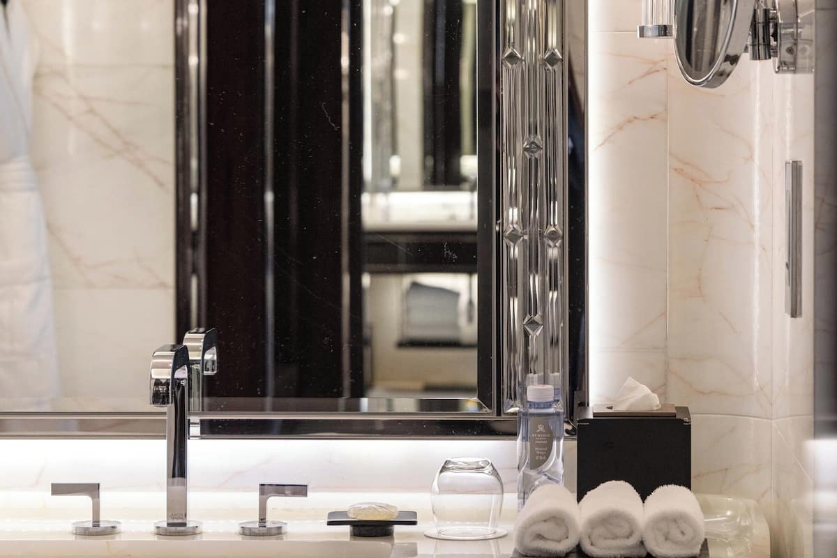 A modern bathroom with a large mirror, a sink with multiple faucets, and a towel rack with towels.